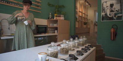 Hanf-Shops - Produktkategorie: CBD-Produkte - Frau mit grünem Oberteil rührt einen Kaffee in einem Café an. - Charlie Green GmbH 