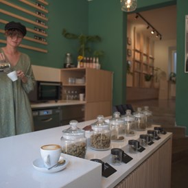 CBD-Shop: Frau mit grünem Oberteil rührt einen Kaffee in einem Café an. - Charlie Green GmbH 
