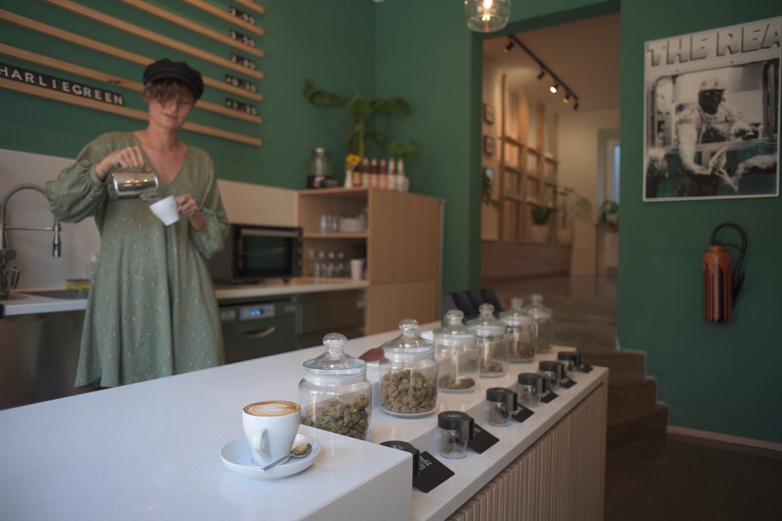 CBD-Shop: Frau mit grünem Oberteil rührt einen Kaffee in einem Café an. - Charlie Green GmbH 